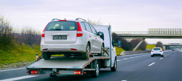 Minivan car with low tow trailer in road. Mini van auto vehicle with Carrier transporter hauler on driveway. European transport logistics at haulage work transportation. Haul with driver on highway.